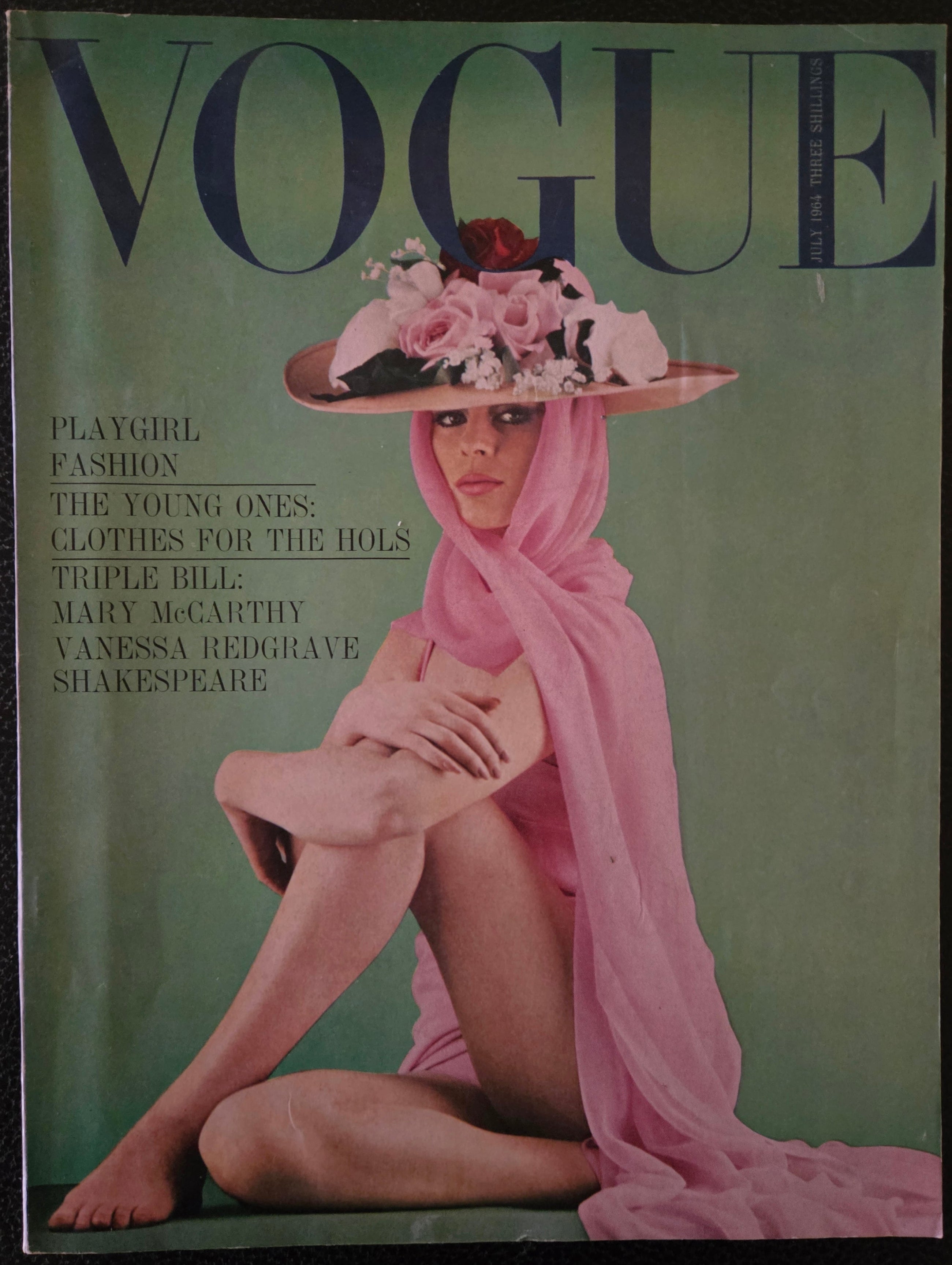 Vintage Vogue magazine cover with a model in a pink dress and hat on a green background
