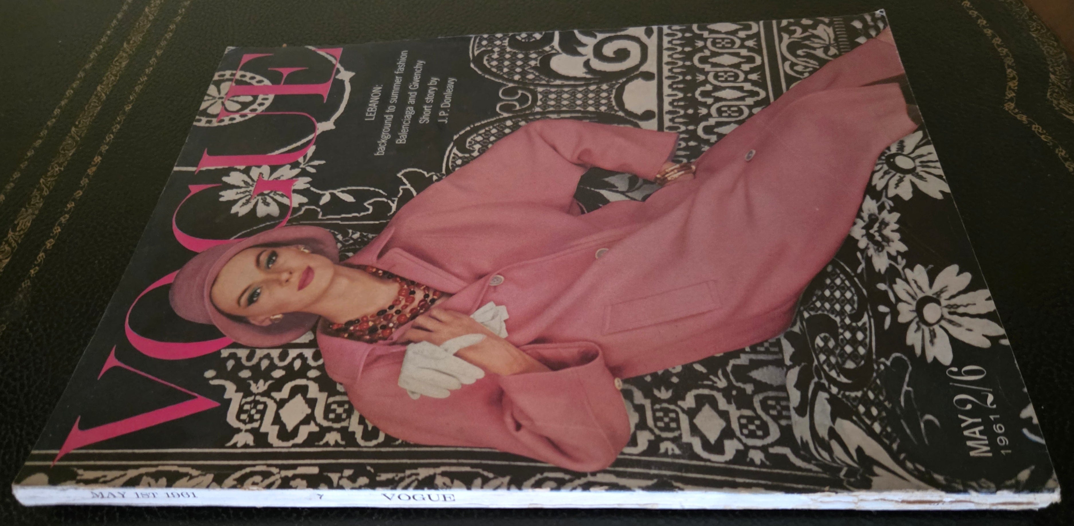 Vogue magazine cover with a model in a pink coat on a dark surface