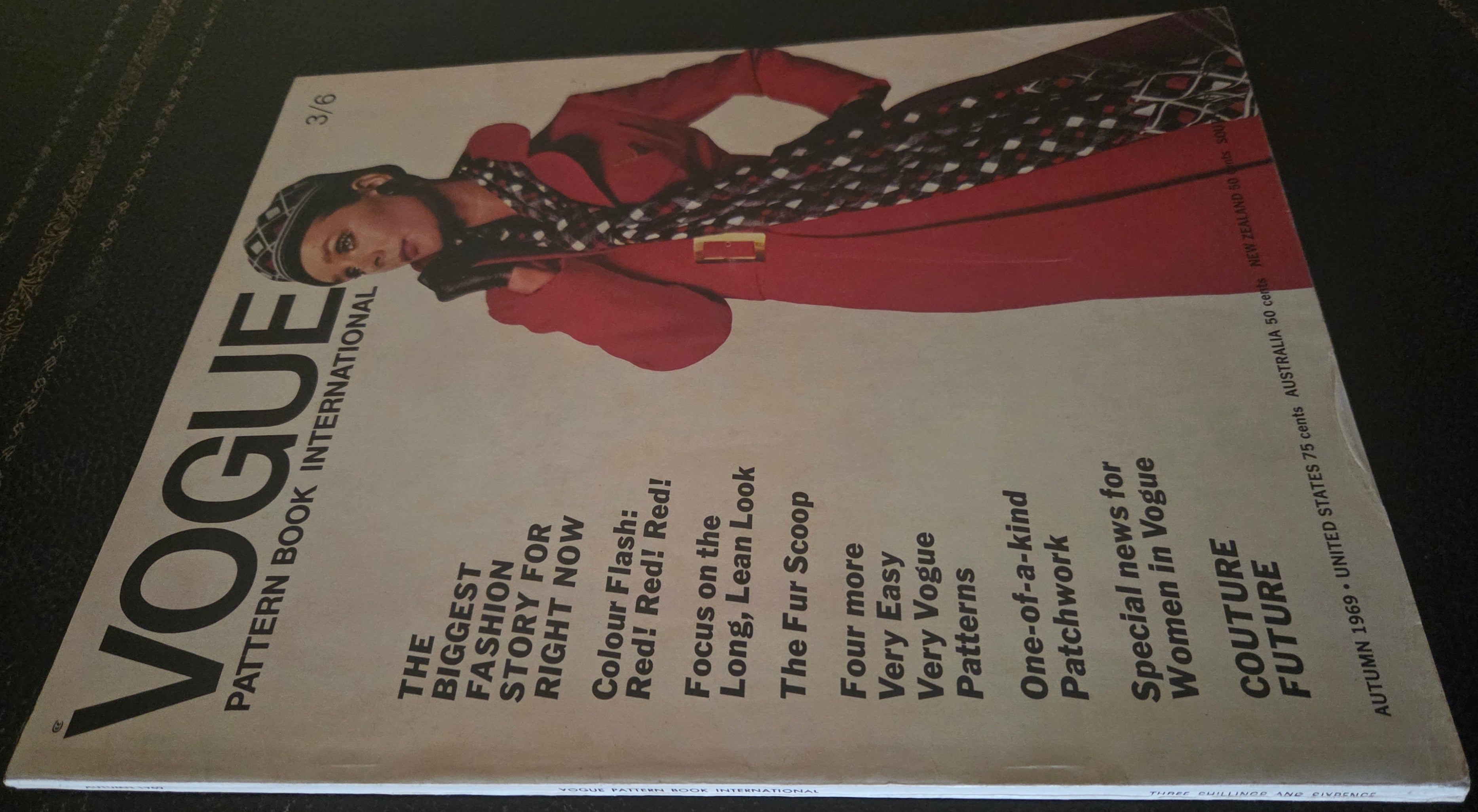 Vintage Vogue magazine cover with a model wearing a red coat and patterned scarf on a dark surface.