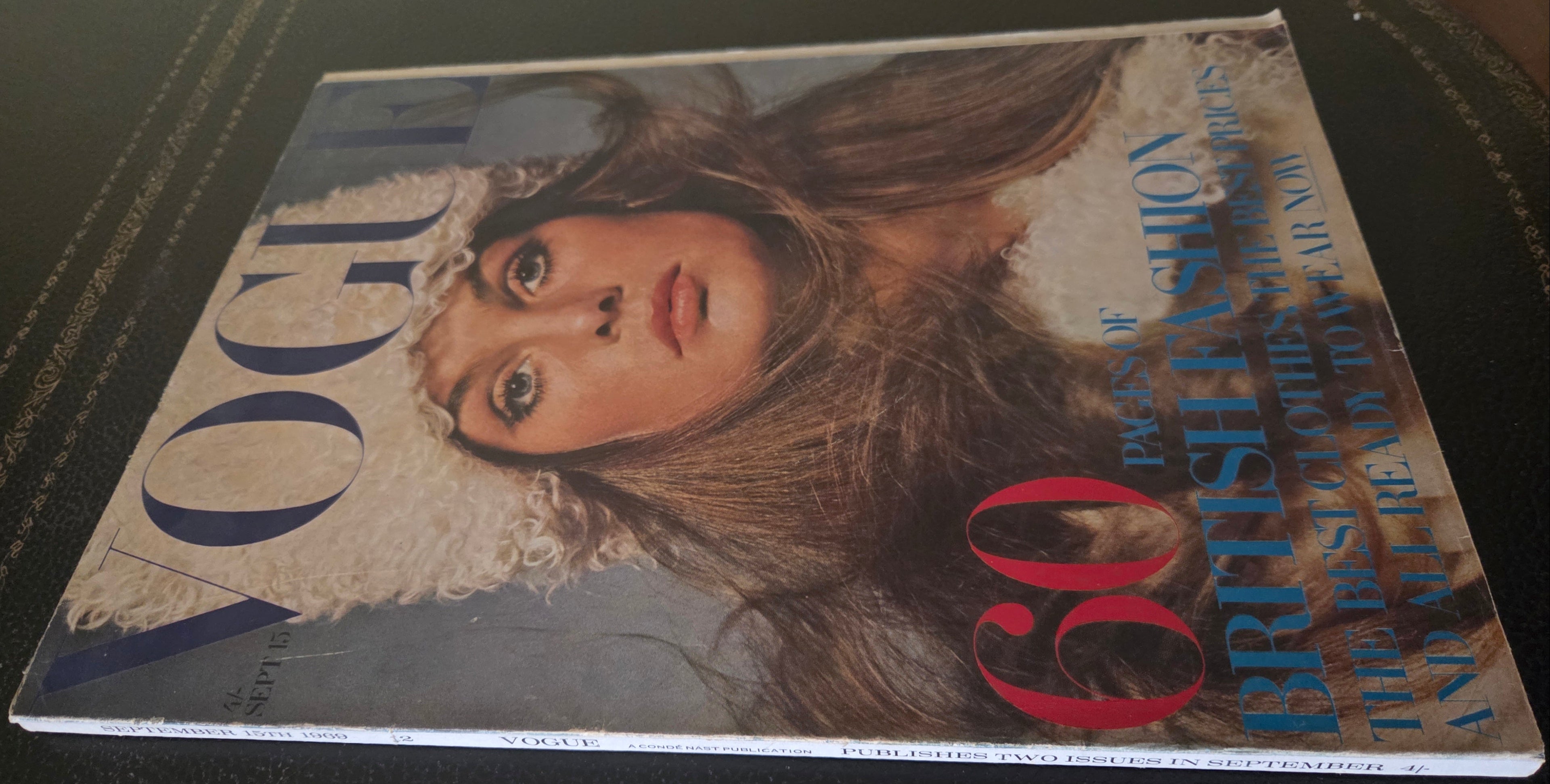 Vintage Vogue magazine with a cover featuring a model wearing a hat on a dark surface